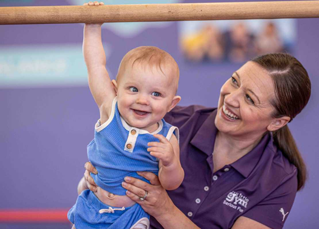 the little gym instructor supporting an infant boy holding onto a bar