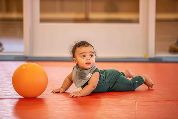 baby laying on the floor in front of an orange ball