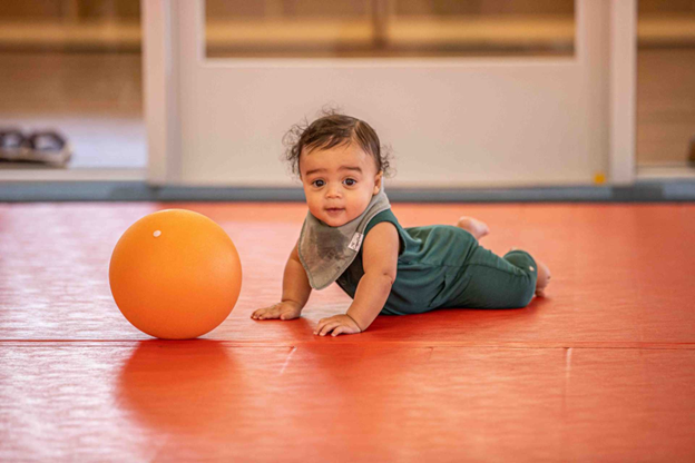 infant laying in front of an orange ball