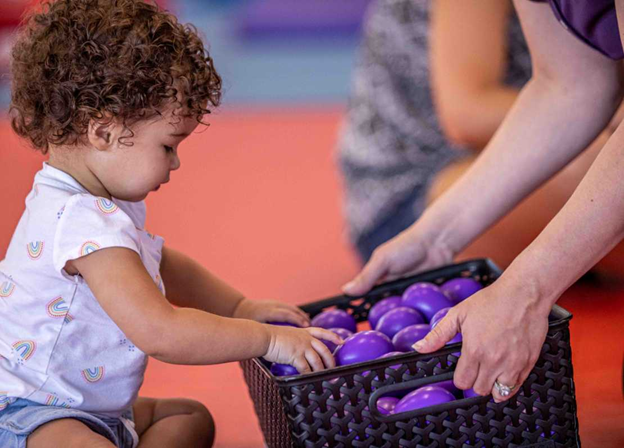 infant in front of a basket filled with purple balls