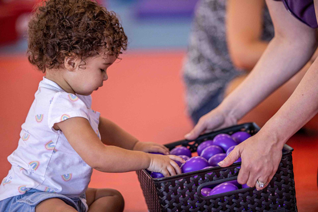  a baby sitting in front of a basket with purple balls